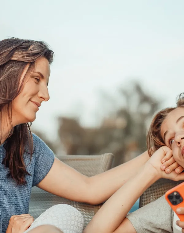 Une maman sourit tendrement à son fils adolescent, téléphone à la main