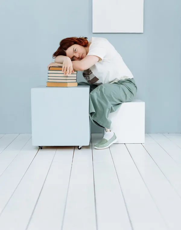 Une jeune femme épuisée, la tête posée sur une pile de livres