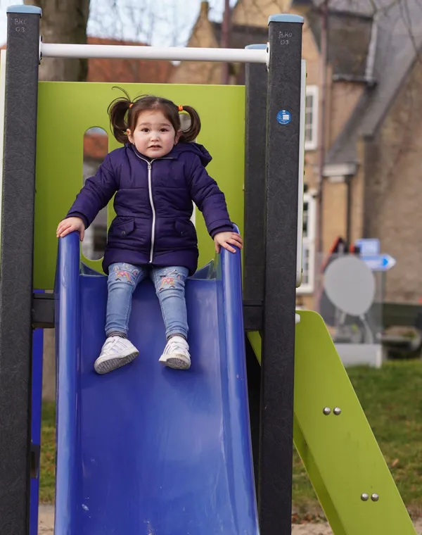 Une petite fille assise en haut d’un toboggan, au parc