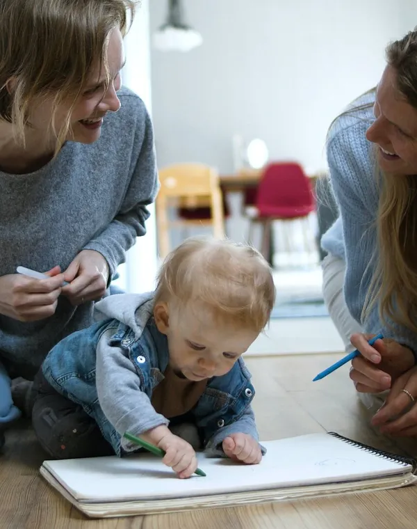 Deux mamans souriantes regardent leur bébé dessiner