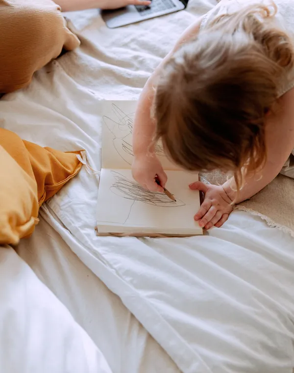 Un parent travaille sur son ordinateur pendant que son enfant dessine à côté